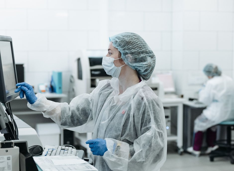 Técnica de laboratorio con barbijo y guantes operando una pantalla de equipamiento, entorno de salud y farma