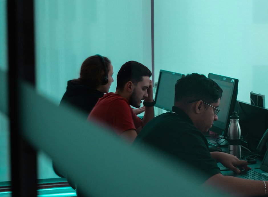 Equipo de soporte técnico trabajando en sus puestos, con auriculares y computadoras, atendiendo a clientes de forma remota